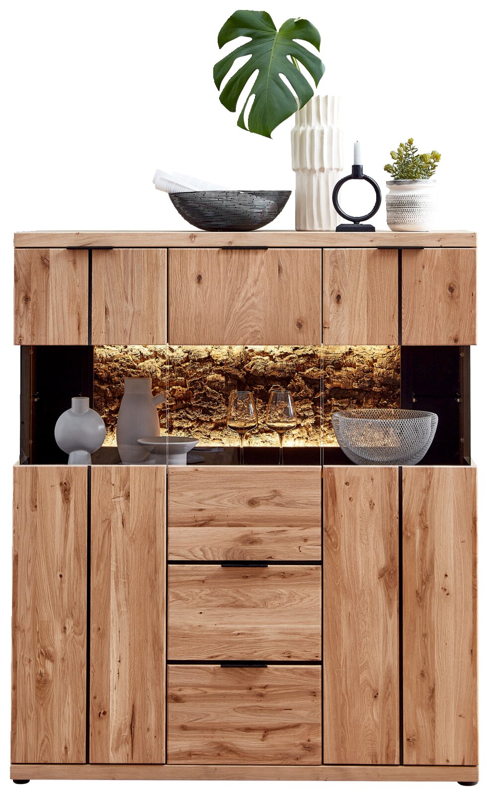 Cantus Highboard DONNA Frontansicht einer modernen Massivholz-Kommode/Sideboard aus Eiche mit Glasvitrine und warm beleuchtetem Steinrückwand-Fach, dekoriert mit Vasen, Schalen, Kerzenhalter und Pflanze
