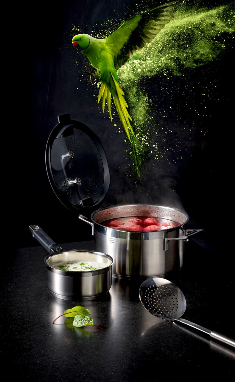 Topfset SILENCE PRO aus Edelstahl mit dampfendem Topf und fliegendem grünem Papagei, seitliche Perspektive