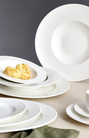 Elegantes weißes Tafelset mit feiner Struktur, bestehend aus tiefen und flachen Tellern, aus seitlicher Perspektive fotografiert.