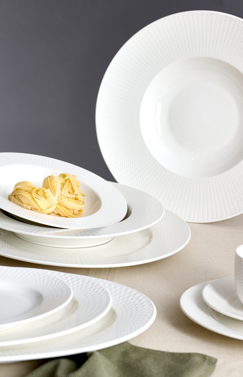 Elegantes weißes Tafelset mit feiner Struktur, bestehend aus tiefen und flachen Tellern, aus seitlicher Perspektive fotografiert.