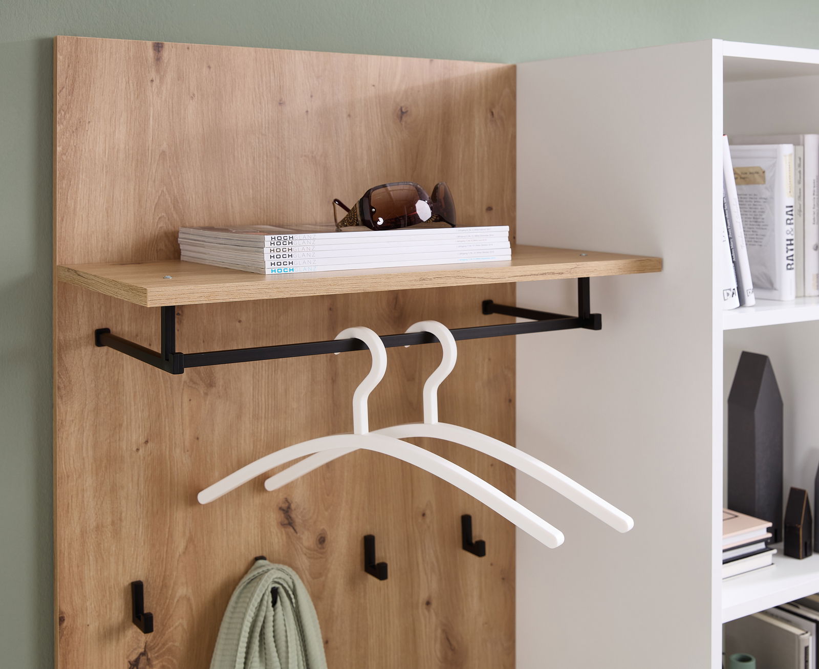 Kompaktgarderobe aus Holz mit schwarzem Metallgestell, zwei weißen Kleiderbügeln und Ablage für Accessoires, seitliche Perspektive