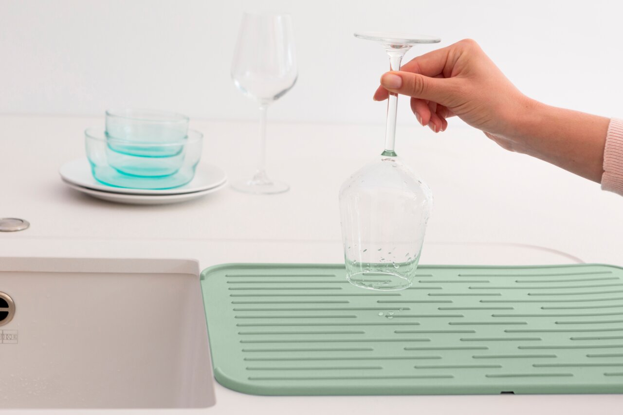 Silikon Abtropfmatte in mintgrün auf einer Küchenarbeitsplatte, mit einem umgedrehten Weinglas darauf. Perspektive von oben.
