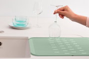 Silikon Abtropfmatte in mintgrün auf einer Küchenarbeitsplatte, mit einem umgedrehten Weinglas darauf. Perspektive von oben.