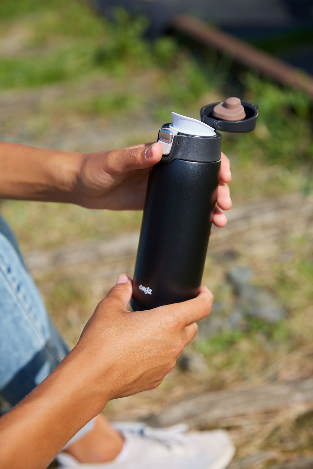 Schwarzer Thermobecher mit geöffnetem Deckel, in der Hand gehalten, im Freien.