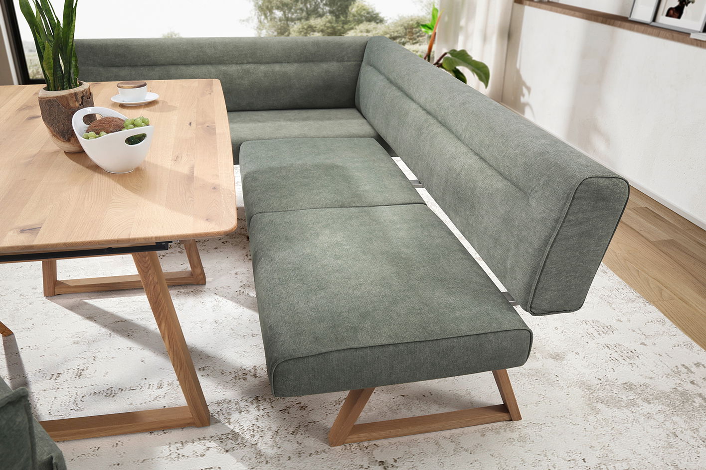 Moderne Eckbank in grauem Stoff mit Holzbeinen, neben einem Esstisch aus Holz, aus der Vogelperspektive fotografiert.