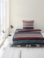 Bettwäsche-Set mit bunten Streifen auf einem Palettenbett, fotografiert aus der Vorderansicht in einem hellen Raum mit Fenster und Stehlampe.