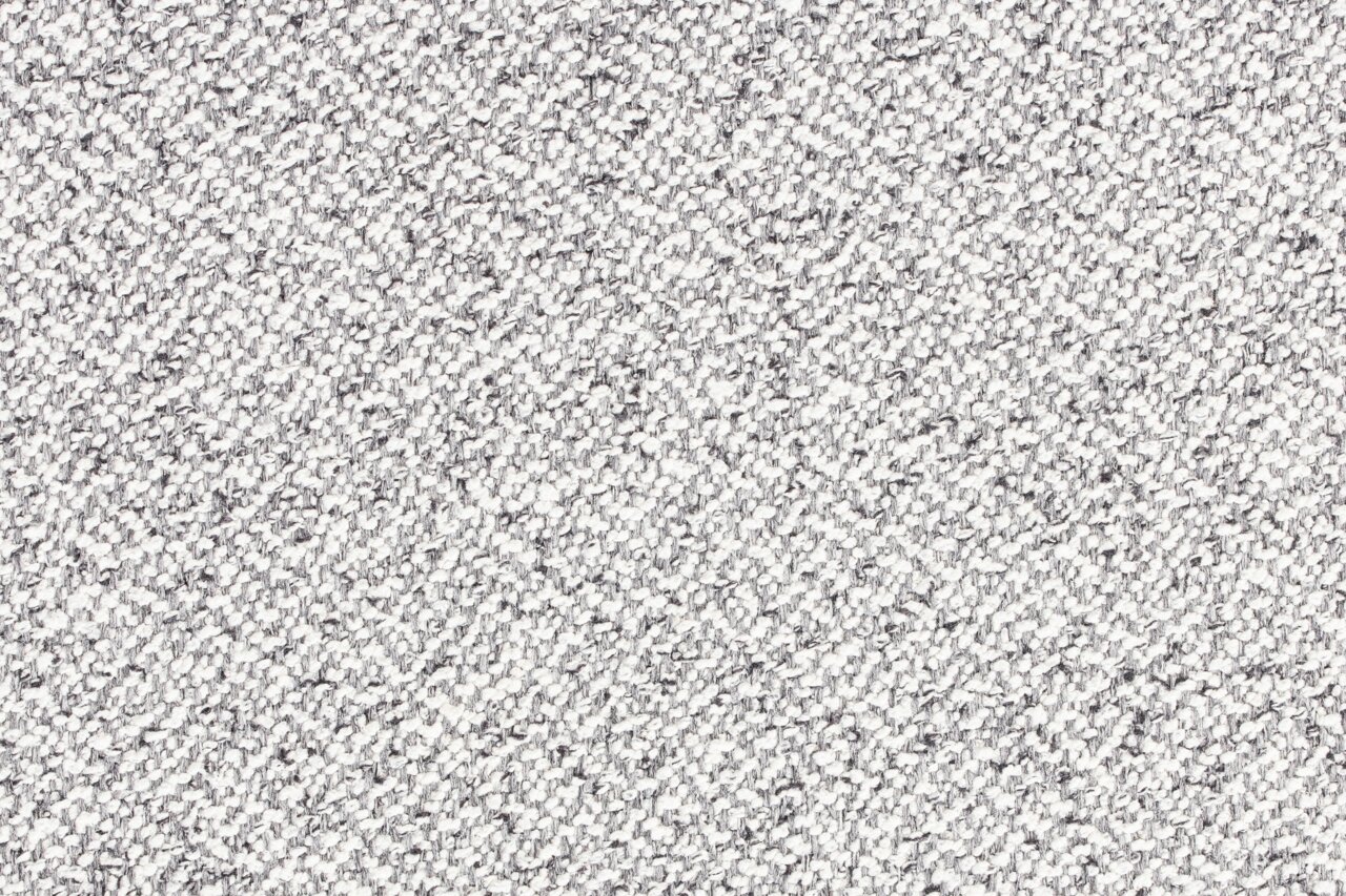 Nahaufnahme der grauen, strukturierten Stoffoberfläche des Hockers MILOU.