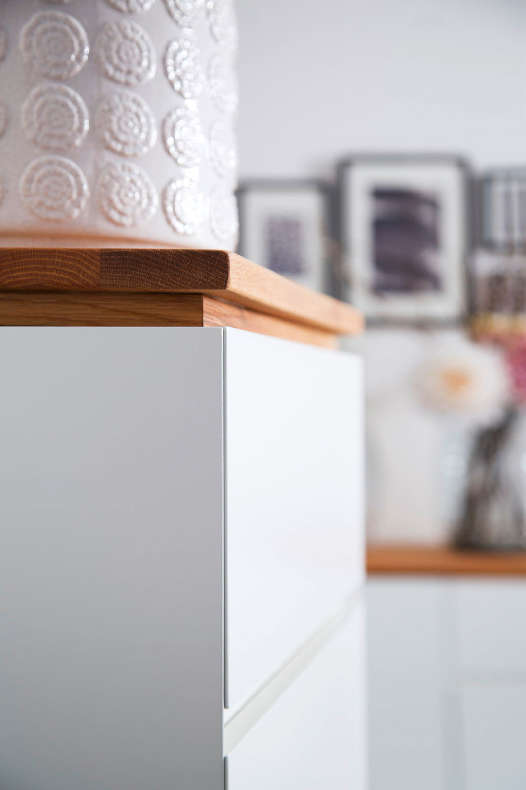 Nahaufnahme einer weißen Hochkommode mit Holzplatte, seitliche Perspektive