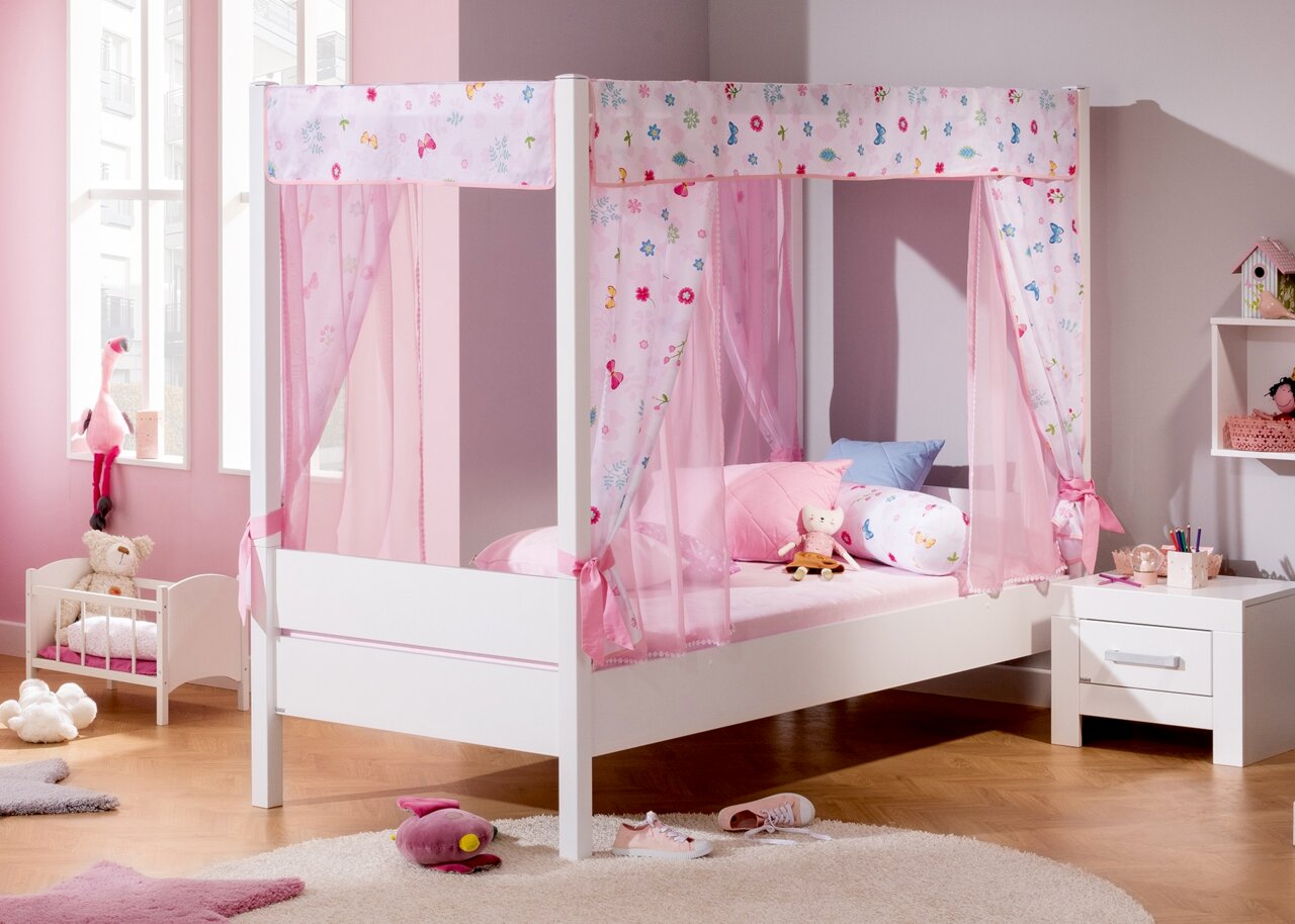 Weißes Kinderbett mit rosa Vorhängen und bunten Kissen, seitliche Perspektive