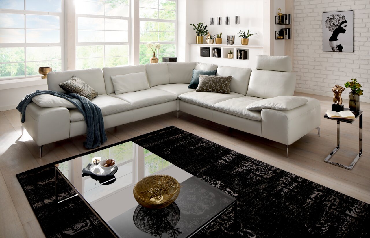 Moderne weiße Polsterrundecke in einem hellen Wohnzimmer mit großen Fenstern, dekoriert mit Kissen und einer Decke, aus der Perspektive von vorne links.