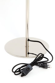 Nahaufnahme der Basis einer Tischleuchte mit glänzendem Metallfuß und schwarzem Kabel mit Schalter, seitliche Perspektive.