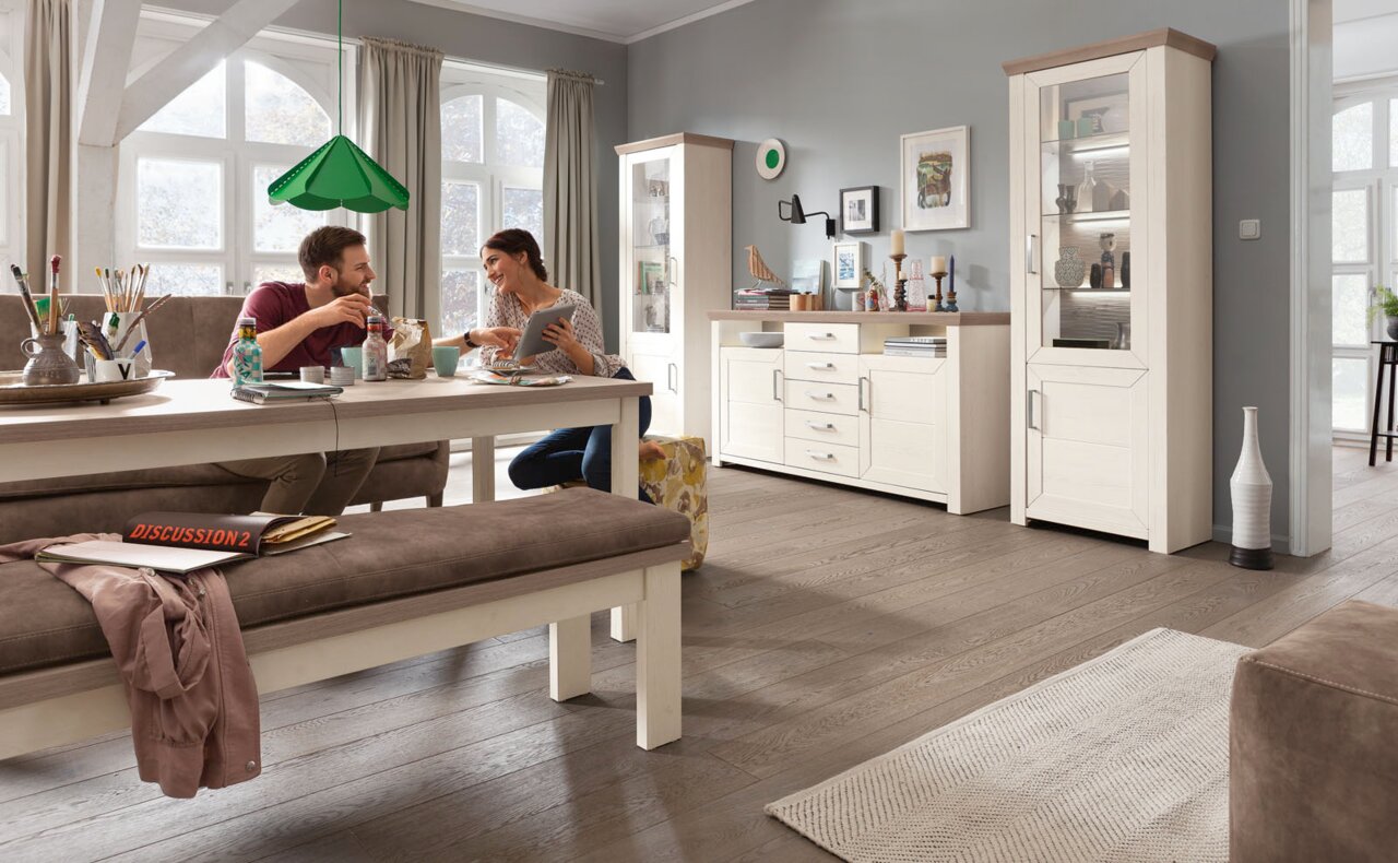 Gemütliches Esszimmer mit Esstisch, Bank und Vitrine in heller Holzoptik, seitliche Perspektive.