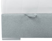 Close-up van een boxspring met grijze stoffen bekleding en een wit matras, gezien vanaf de zijkant