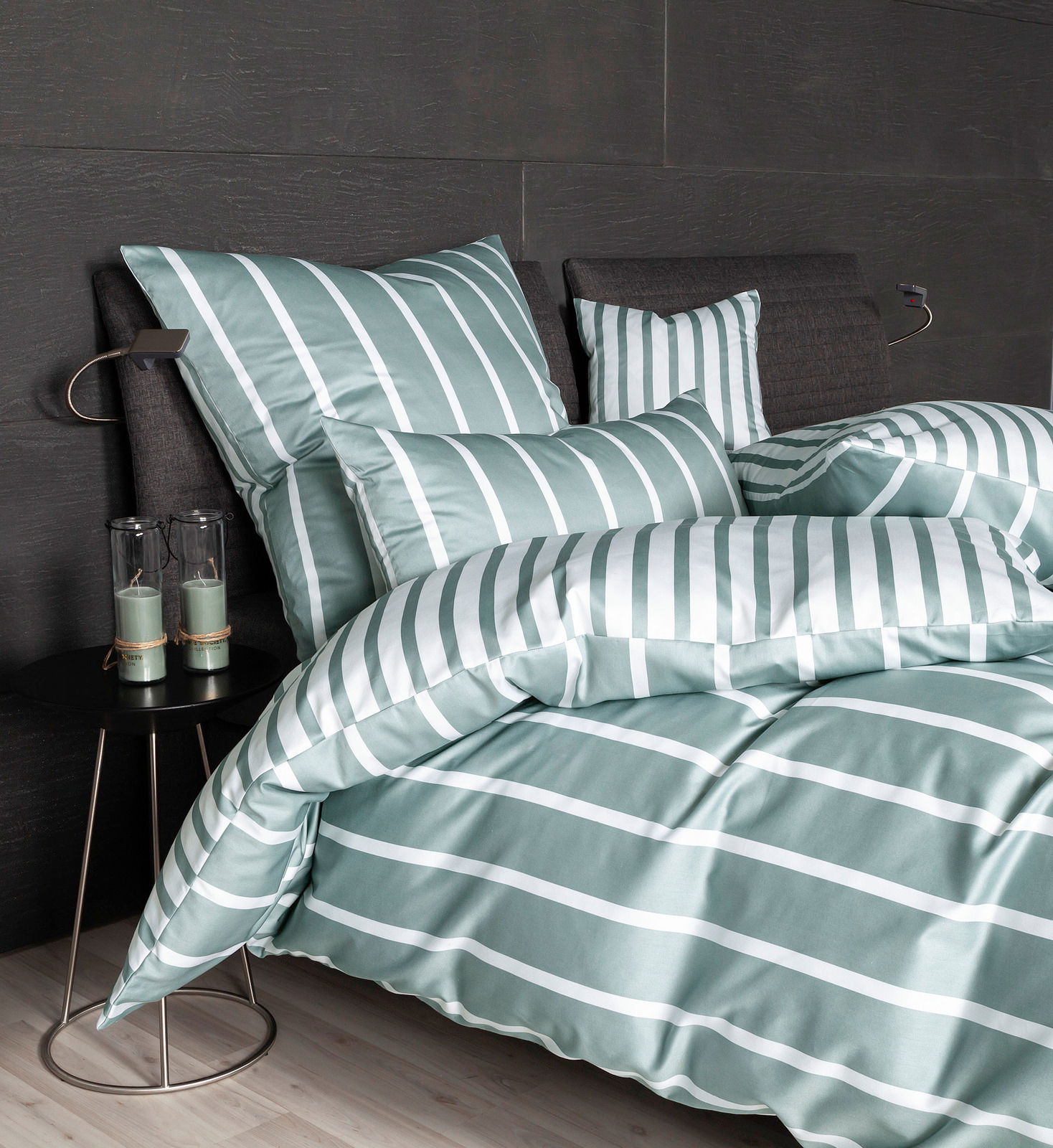 Bettwäsche-Set in grün-weißem Streifenmuster auf einem Bett mit dunklem Kopfteil, seitliche Perspektive