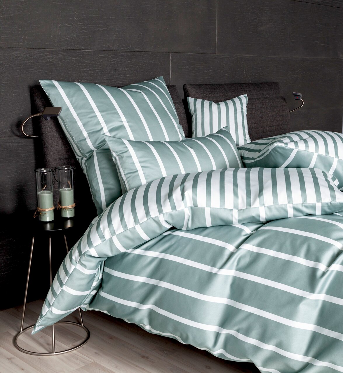 Bettwäsche-Set in grün-weißem Streifenmuster auf einem Bett mit dunklem Kopfteil, seitliche Perspektive