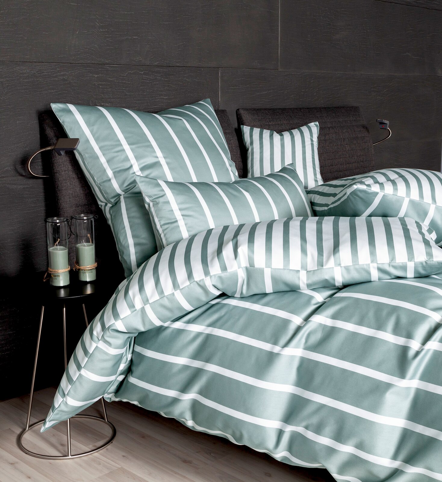 Bettwäsche-Set in grün-weißem Streifenmuster auf einem Bett mit dunklem Kopfteil, seitliche Perspektive