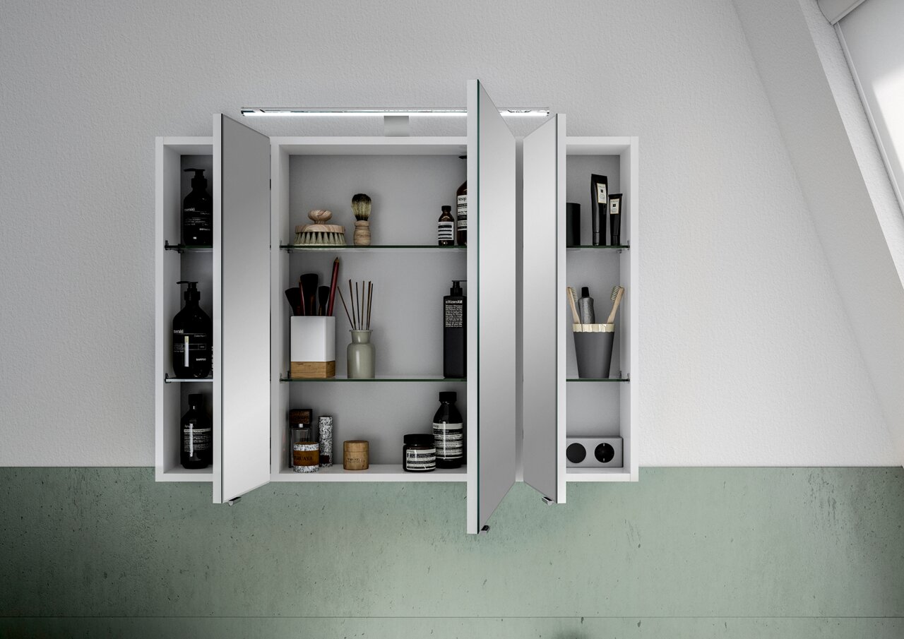 Spiegelschrank mit geöffneten Türen, gefüllt mit Pflegeprodukten und Accessoires, aus frontaler Perspektive.