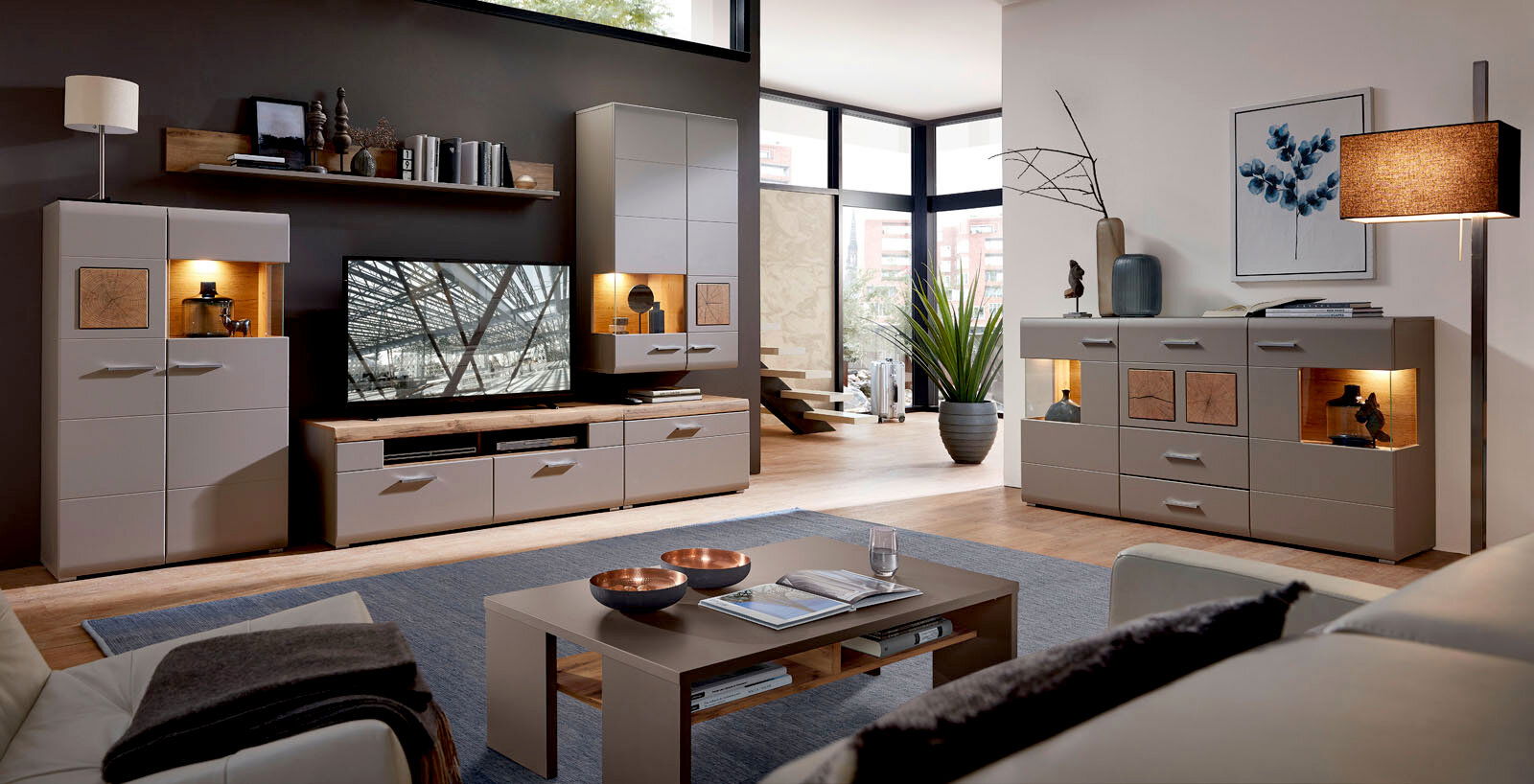 Moderne Wohnwand mit TV-Schrank, Couchtisch und Sideboard in einem stilvollen Wohnzimmer mit großen Fenstern, seitliche Perspektive.