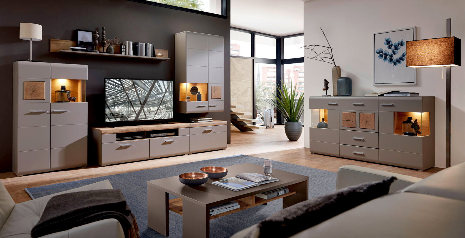 Moderne Wohnwand mit TV-Schrank, Couchtisch und Sideboard in einem stilvollen Wohnzimmer mit großen Fenstern, seitliche Perspektive.