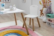 Weißer Kinderstuhl mit Holzbeinen neben passendem weißem Tisch im Kinderzimmer, seitliche Perspektive auf Sitzfläche und Rückenlehne