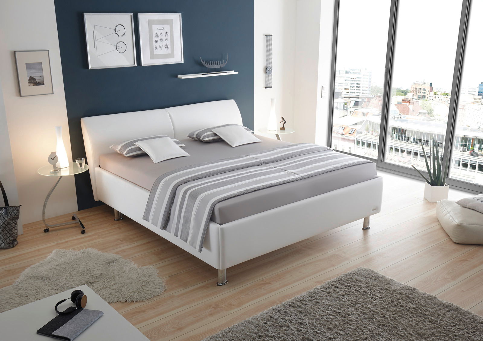 Modernes Polsterbettgestell in einem stilvollen Schlafzimmer mit Blick auf die Stadt durch große Fenster, seitliche Perspektive.