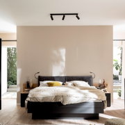 Modernes Schlafzimmer mit Doppelbett und dunklem Bettrahmen, Stoff-Kopfteil, heller Bettwäsche und Decken-Spotleiste an der Decke; frontale Ansicht auf das Bett