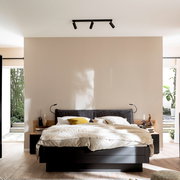 Modernes Schlafzimmer mit Doppelbett und dunklem Bettrahmen, Stoff-Kopfteil, heller Bettwäsche und Decken-Spotleiste an der Decke; frontale Ansicht auf das Bett