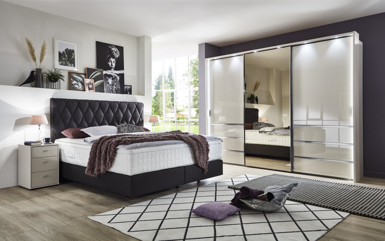 Slaapkamer met moderne kast met schuifdeuren MALIBU in hoogglans, links een bed met gestoffeerd hoofdeinde, gezien van voren.