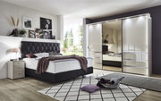 Slaapkamer met moderne kast met schuifdeuren MALIBU in hoogglans, links een bed met gestoffeerd hoofdeinde, gezien van voren.