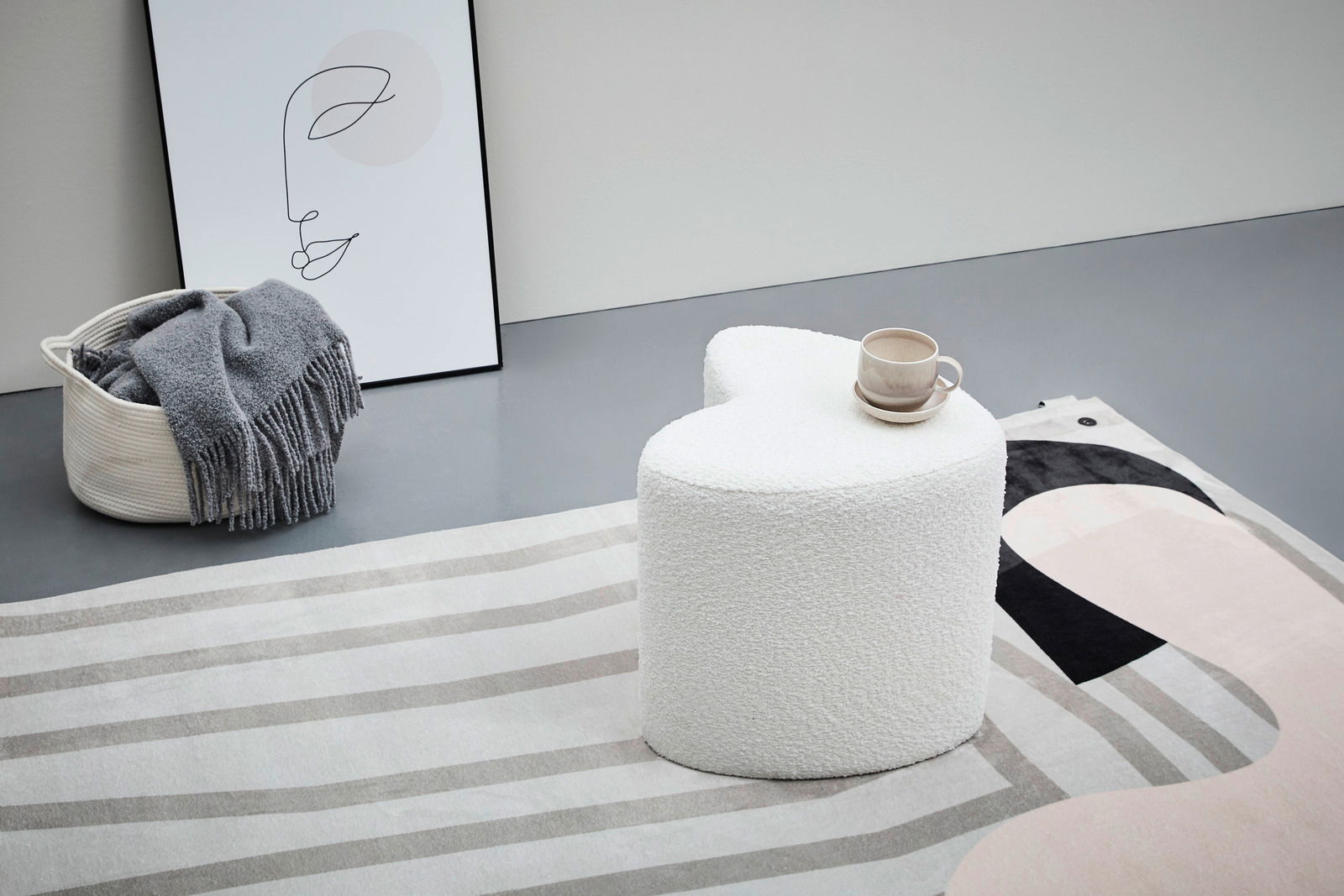 Moderner weißer Hocker in Herzform, seitliche Perspektive, auf einem gemusterten Teppich mit einer Tasse darauf.
