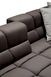 Nahaufnahme einer grauen Longchairkombination mit weichen, gepolsterten Kissen und einem modernen Design, seitliche Perspektive.