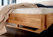 Massivholzbettgestell aus hellem Holz, seitliche Perspektive, mit Bettdecke und Kissen.