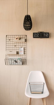 Wandklok Flip No Case in een modern interieur, aan de voorkant bevestigd aan een houten wand, naast een opbergrek van gaas en een hanglamp.