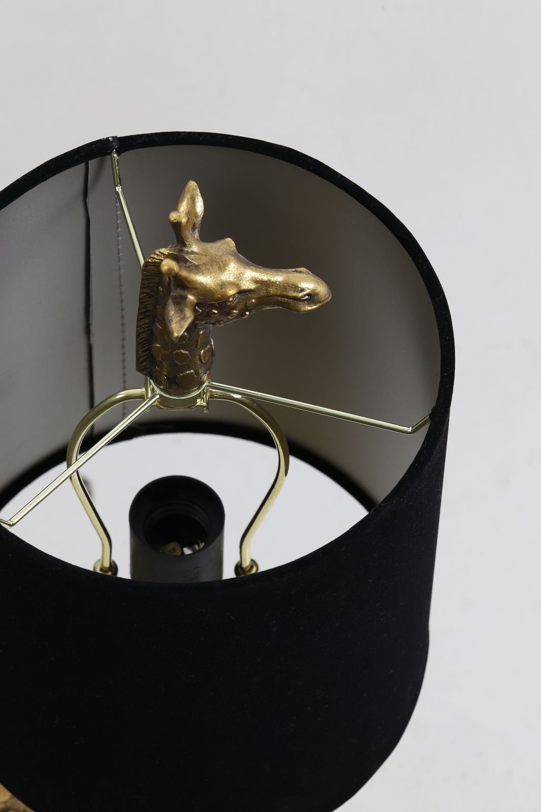 Nahaufnahme einer Tischleuchte mit schwarzem Lampenschirm und einer goldenen Giraffenfigur im Inneren, von oben betrachtet.
