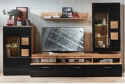 Moderne Wohnwand in Holzoptik mit schwarzen Elementen, bestehend aus mehreren Schränken und Regalen, mit Dekorationen und einem Fernseher in der Mitte, frontal betrachtet.