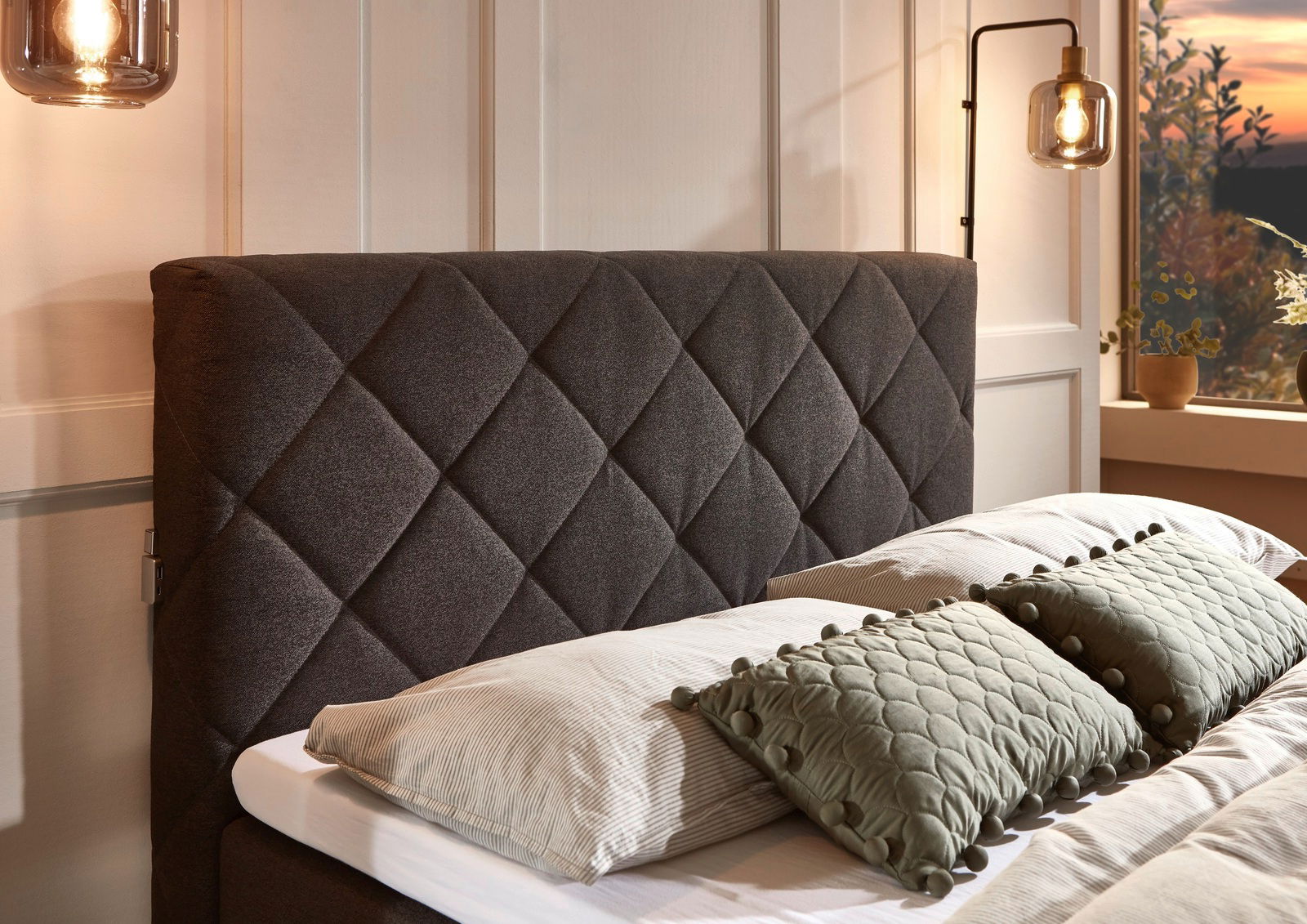 Nahaufnahme eines Boxspringbetts mit gestepptem Kopfteil in einem gemütlichen Schlafzimmer, seitliche Perspektive