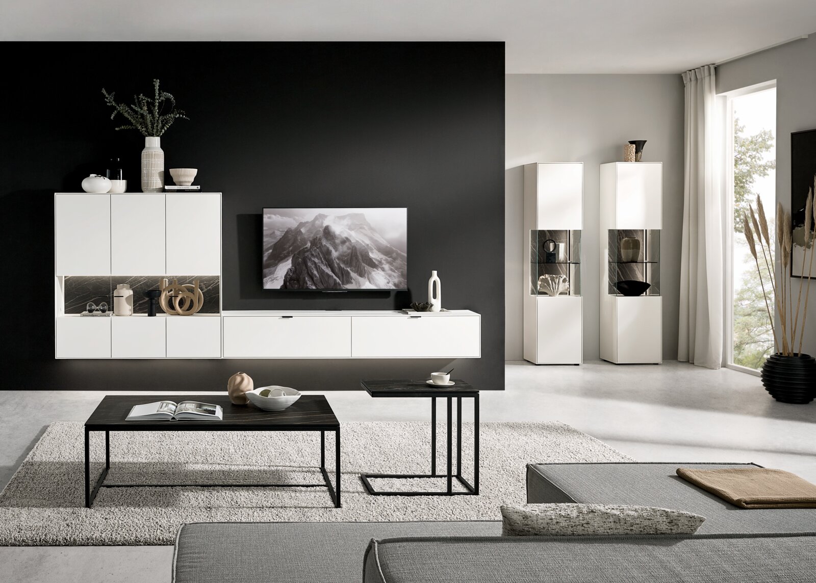 Moderne Wohnzimmerwandkombination in Weiß mit schwarzen Akzenten, bestehend aus Hängeschränken, einem TV-Board und Vitrinen. Perspektive: Frontalansicht.