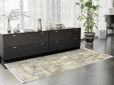 Moderner Designer Teppich in Grün- und Weißtönen auf einem dunklen Fliesenboden, vor einer schwarzen Kommode mit Dekorationen, seitliche Perspektive.