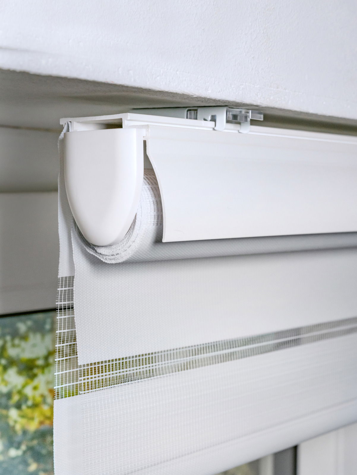 Nahaufnahme eines weißen Doppelrollos mit Blende, montiert an einer Decke, teilweise heruntergelassen.