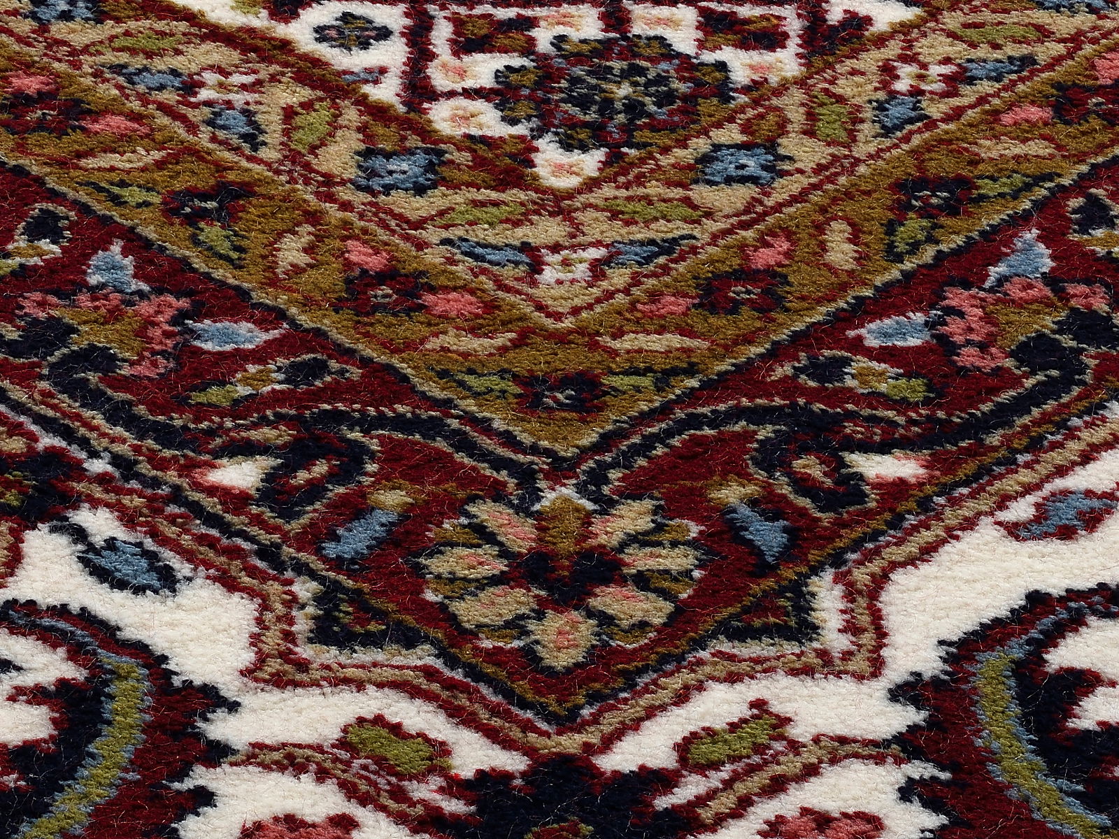 Nahaufnahme eines Orientteppichs mit komplexen Mustern in Rot-, Grün- und Blautönen. Die Perspektive zeigt eine diagonale Ansicht des Teppichs.