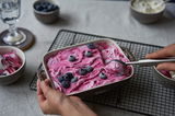 Auflaufform mit pinkem Dessert und Blaubeeren, von oben fotografiert, auf einem Gitter stehend.