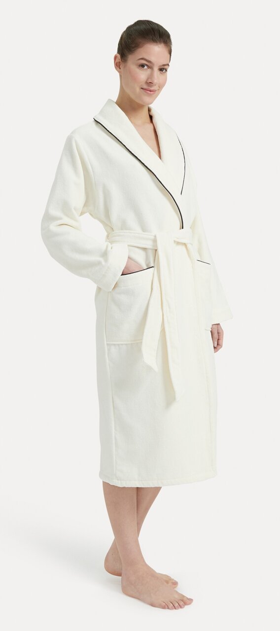 Frau in einem weißen Bademantel mit Schalkragen und schwarzer Paspelierung, von vorne betrachtet.