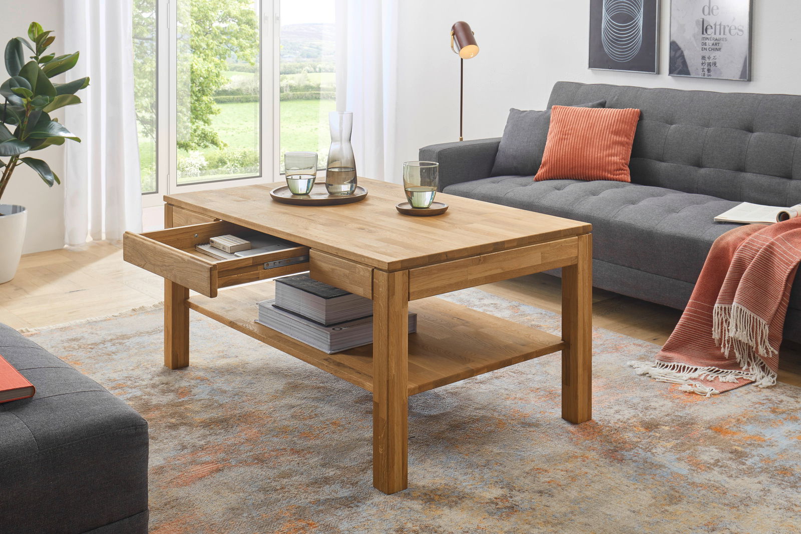Holz-Couchtisch mit Schublade und Ablagefläche, seitliche Perspektive, in modernem Wohnzimmer mit grauem Sofa und orangenem Kissen.