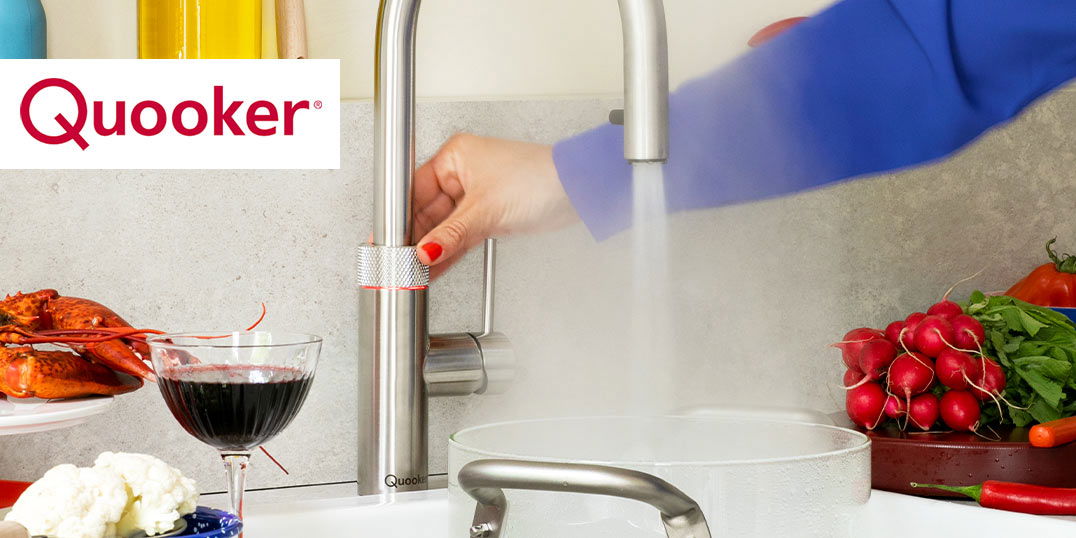 Eine Hand bedient einen Quooker-Wasserhahn und lässt heißes Wasser in einen Topf. Frisches Gemüse und ein Glas Rotwein stehen danaben auf der Arbeitsplatte.