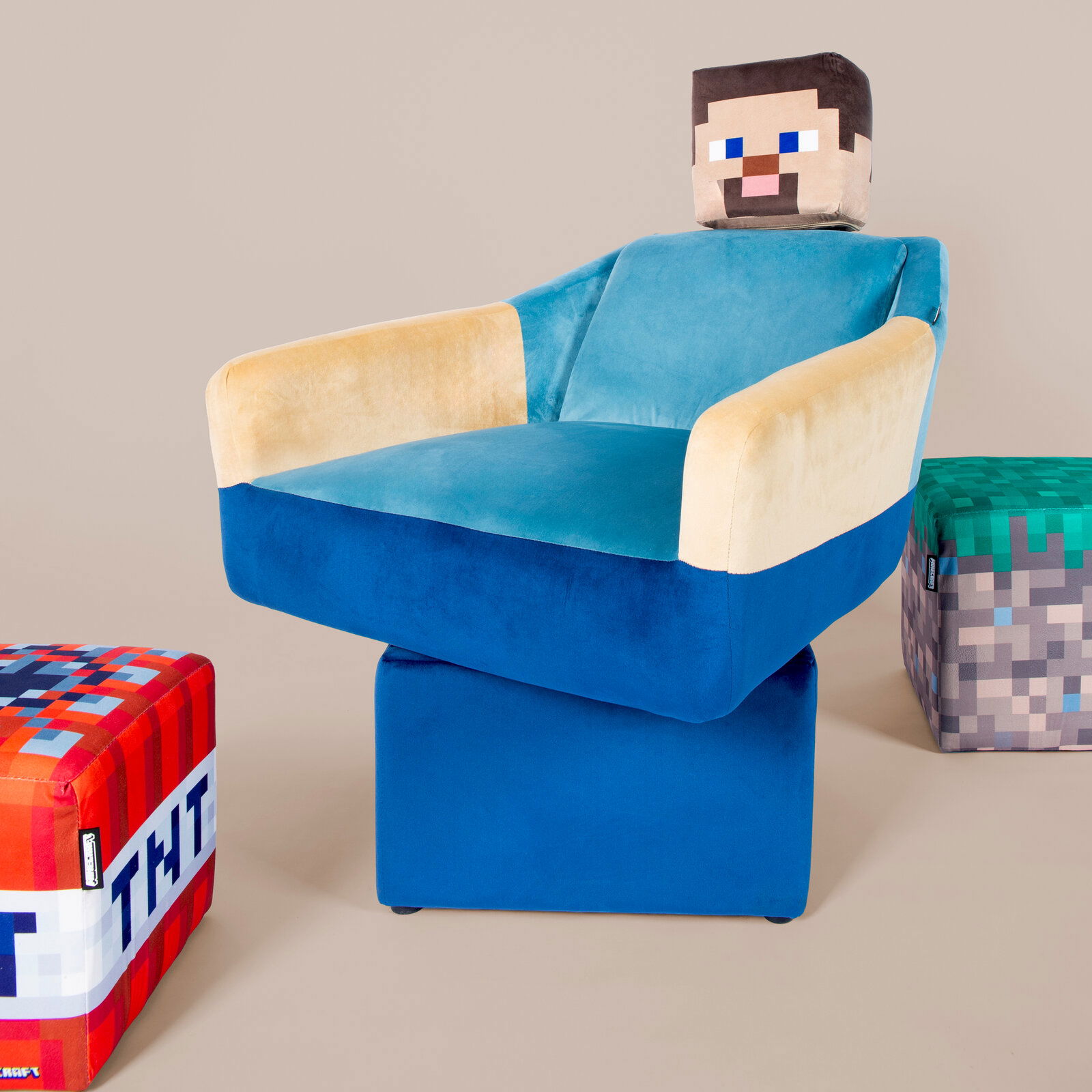 Minecraft-inspirierter, gepolsterter Sessel in Blau und Beige mit würfelförmiger Kopfstütze im Pixel-Design, auf blauem Sockel; Aufnahme in leichter Frontansicht von schräg rechts vor neutralem Hintergrund.