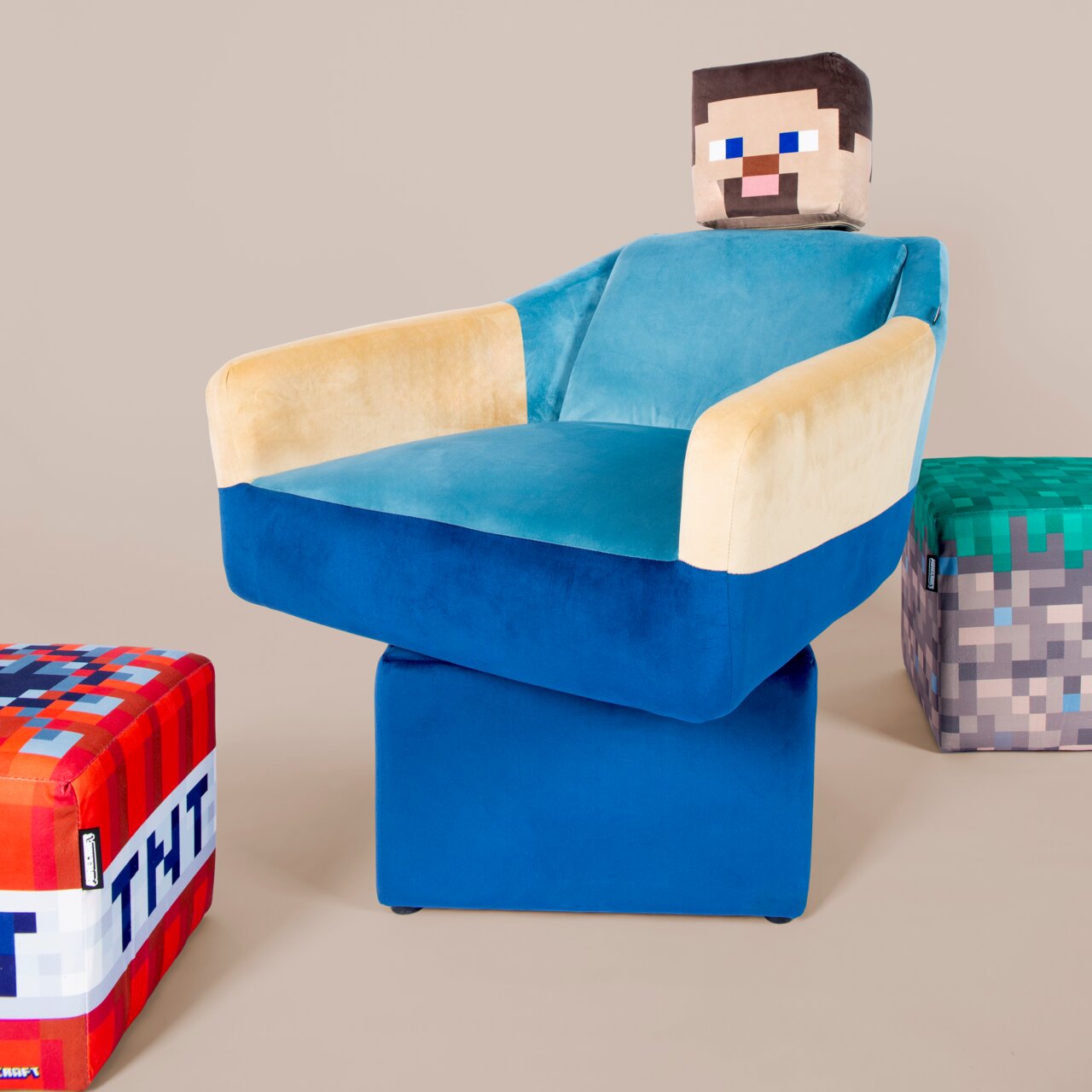 Op Minecraft geïnspireerde, gestoffeerde fauteuil in blauw en beige met een kubusvormige hoofdsteun in pixelstijl, op een blauwe voet; foto in licht vooraanzicht vanuit een schuine hoek rechts tegen een neutrale achtergrond.