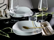 Schwarz gedeckter Tisch mit weißem Porzellan-Geschirr mit gold-schwarzen Linien, goldfarbenem Besteck, Weingläsern und Wasserglas, aufgenommen in schräger Draufsicht.
