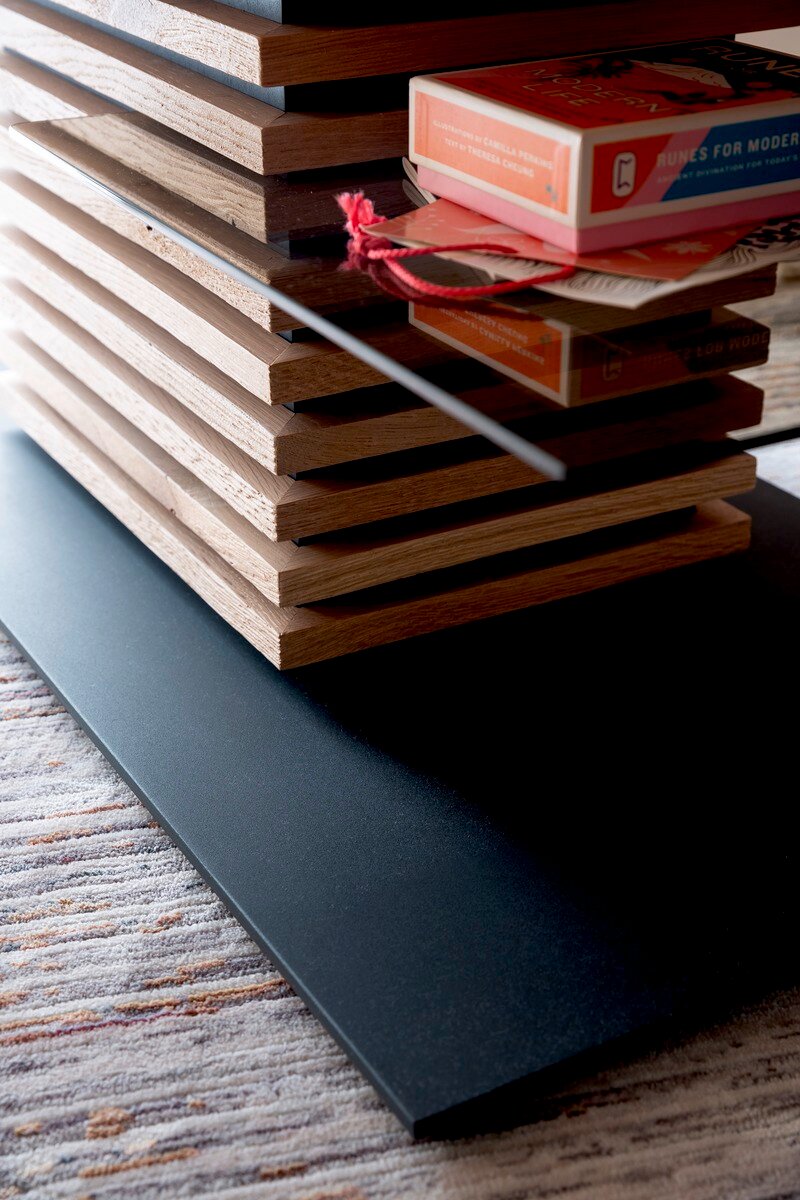 Nahaufnahme eines modernen Couchtisches mit gestapelten Holzelementen und einer Glasplatte, seitliche Perspektive.