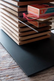 Nahaufnahme eines modernen Couchtisches mit gestapelten Holzelementen und einer Glasplatte, seitliche Perspektive.