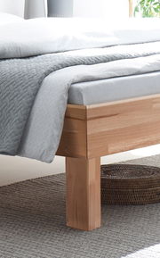 Nahaufnahme eines Bettgestells aus Holz mit einer grauen Bettdecke, seitliche Perspektive